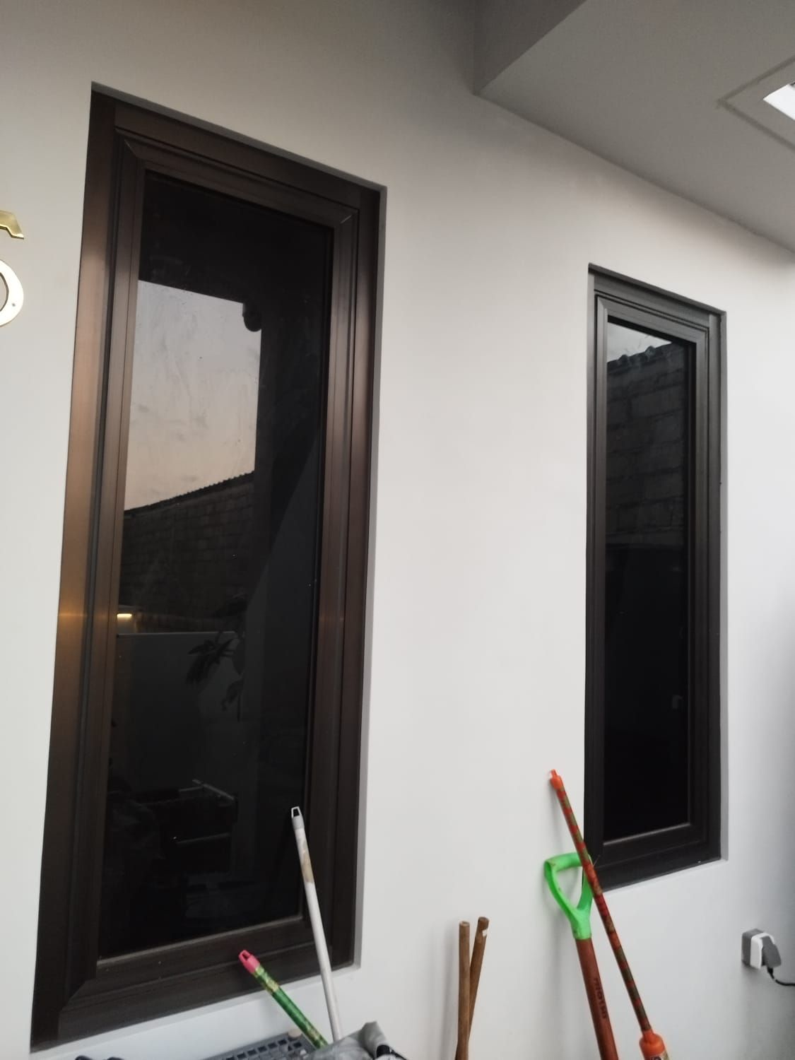 Dua jendela berkusen bronze dilihat dari luar rumah, kaca film hitam membuat kaca tampak gelap dan mengilap